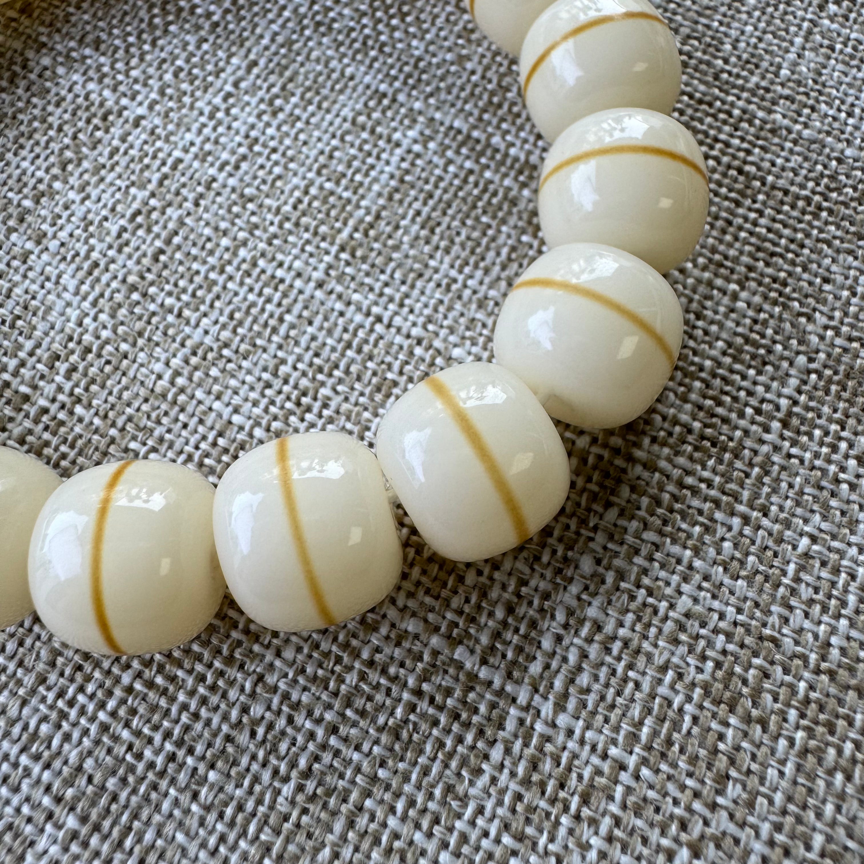 White beads with gold stripes on a textured fabric background