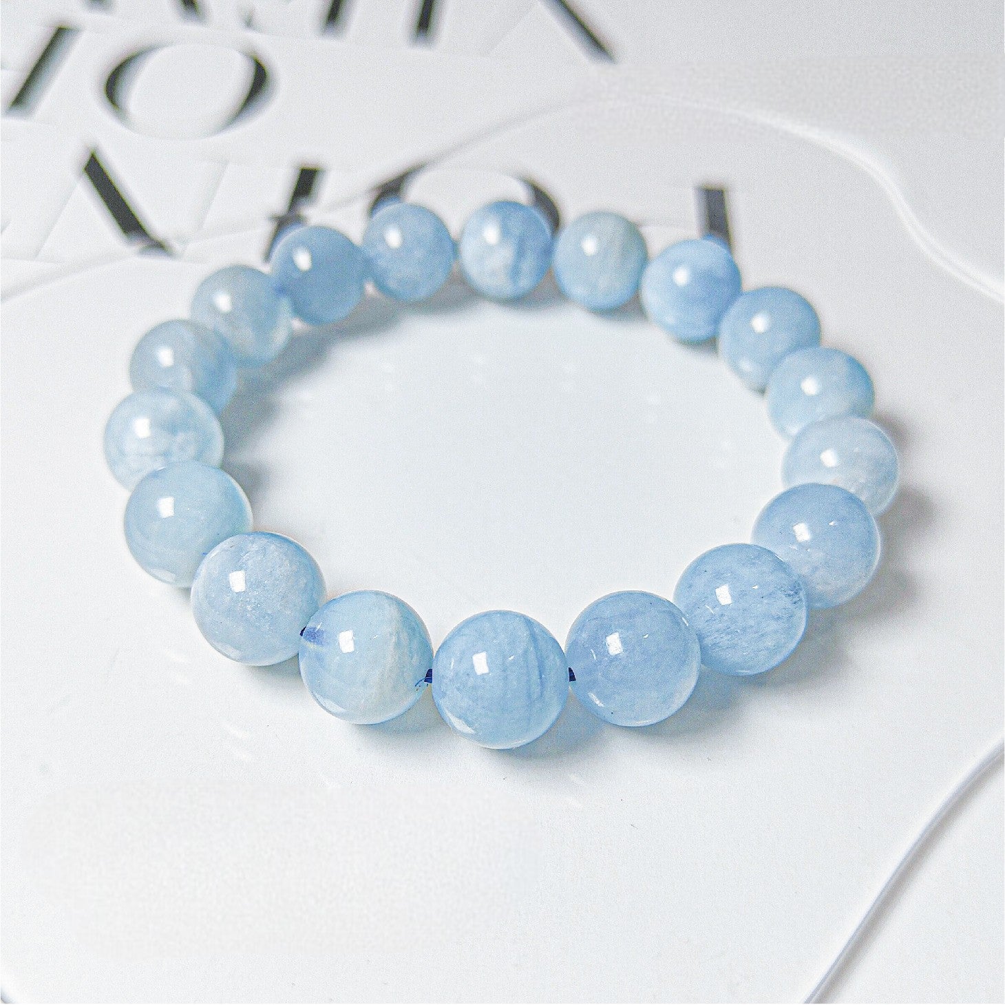Blue beaded bracelet on a white surface with blurred text in the background