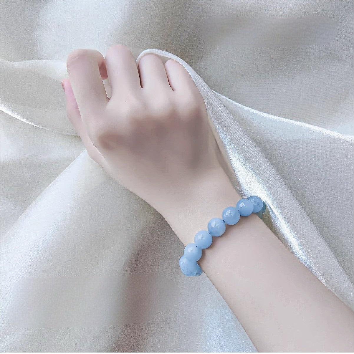Hand wearing a light blue beaded bracelet on a white fabric background