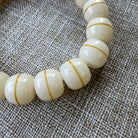 White beads with gold stripes on a textured fabric background